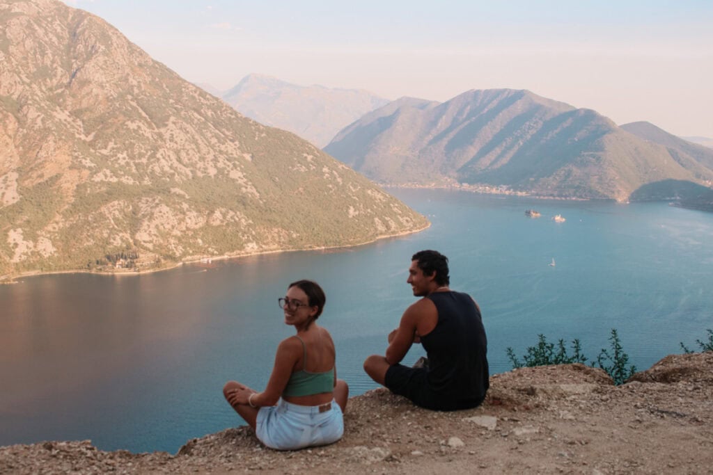 girl and boy sitting with a view of a lake while they travel in Montenegro