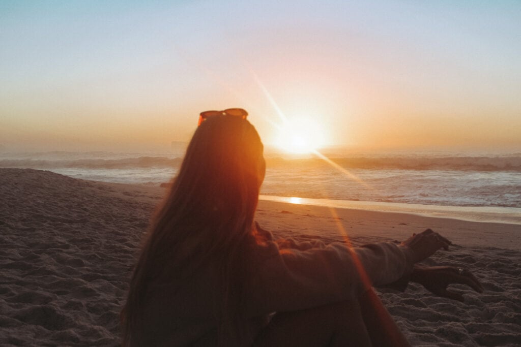 girl sitting on Clifton Beach in Cape Town at sunset in October